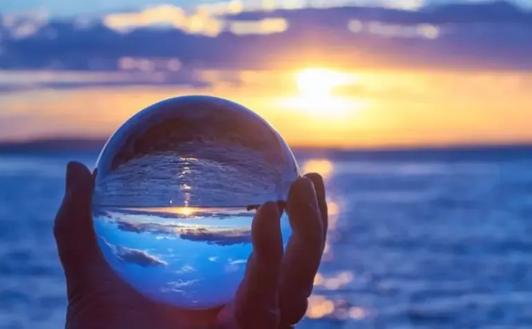 Bola de cristal sostenida frente al mar al atardecer